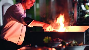 A chef in a white chef's coat and hat cooking with flames on a stove. - Mövenpick Resort & Residences Aqaba (Aqaba)