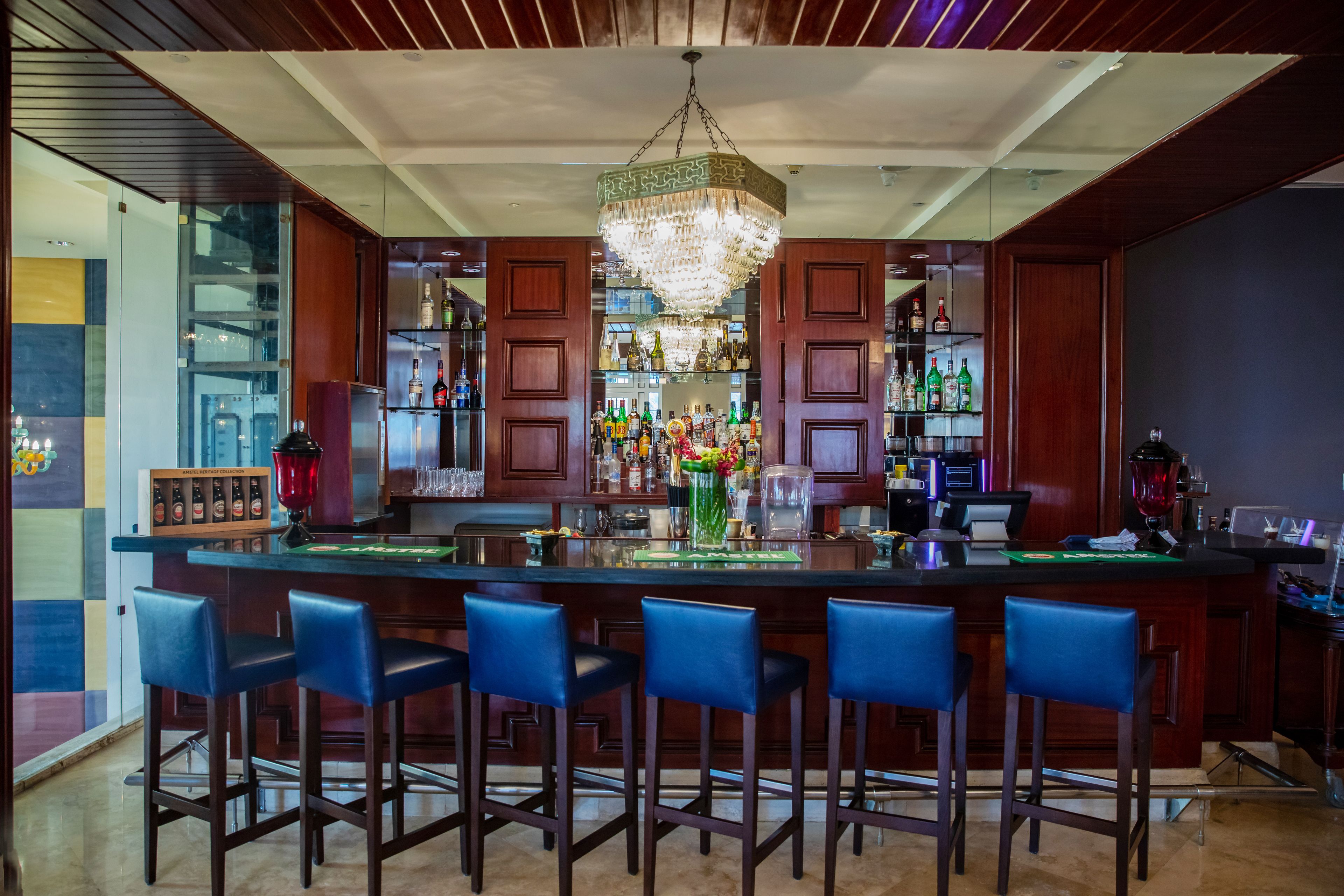 A bar area with a central island, bar stools, and a chandelier.