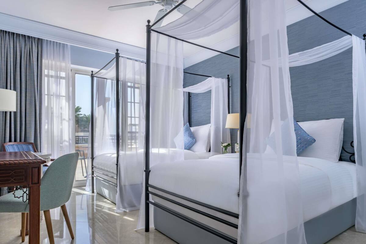 A four-poster bed with sheer curtains, a desk with a chair, and a view of the outdoors.