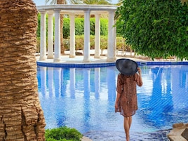 A pool with a clear blue water surface, surrounded by palm trees and a white columned structure.