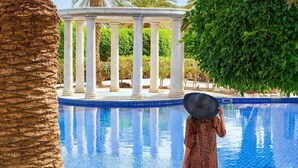 A pool with a clear blue water surface, surrounded by palm trees and a white columned structure. - Mövenpick Resort & Residences Aqaba (Aqaba)
