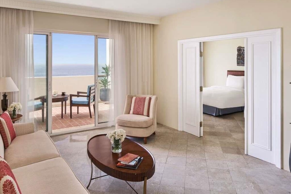 A hotel room with a balcony, a sofa, a chair, a coffee table, and a bed.