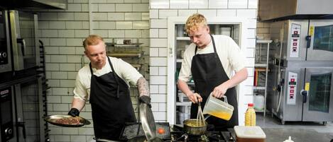 A kitchen with two chefs preparing food, stainless steel appliances, and a tiled backsplash.