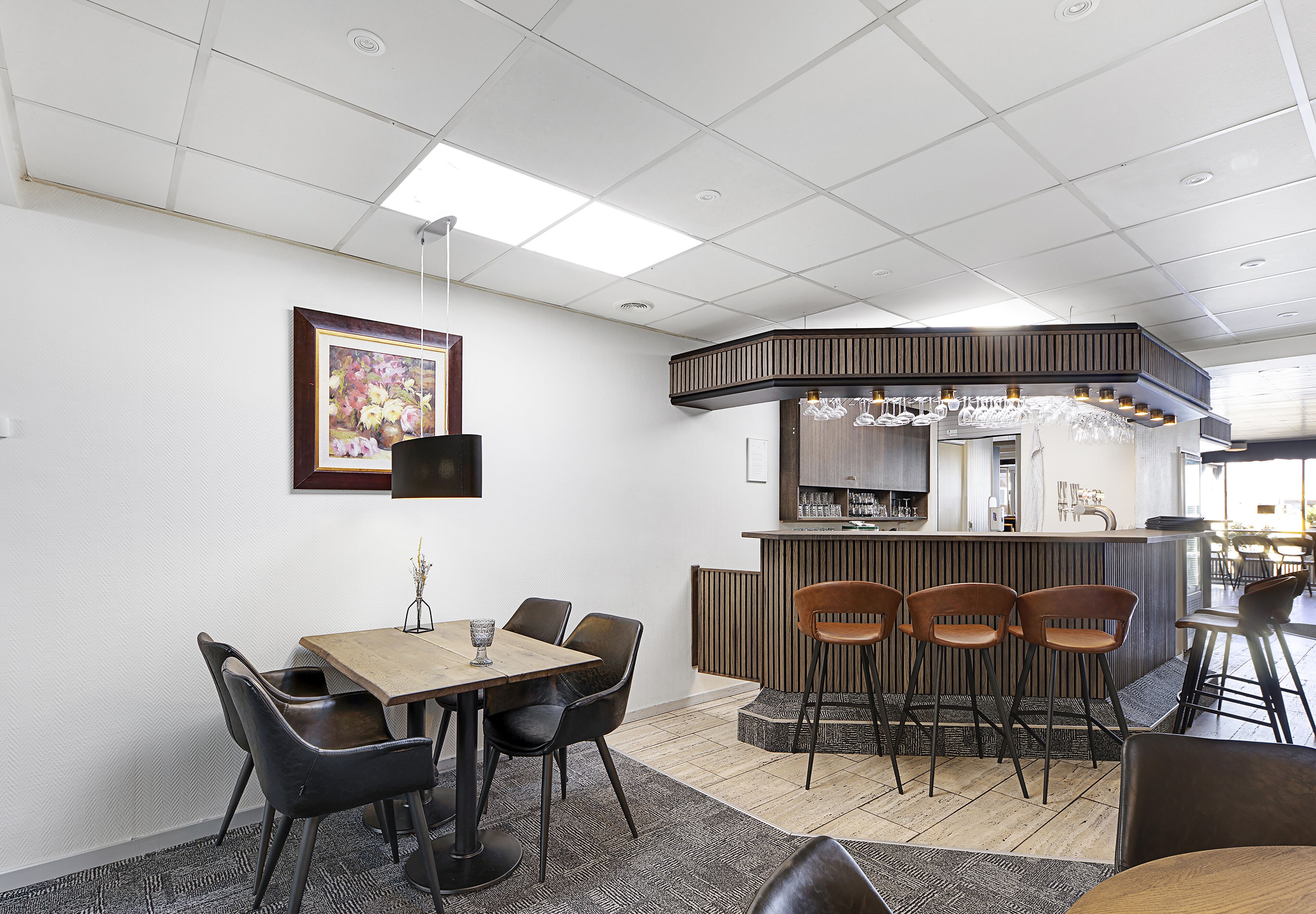 A modern dining area with a wooden table, black chairs, and a bar with stools.