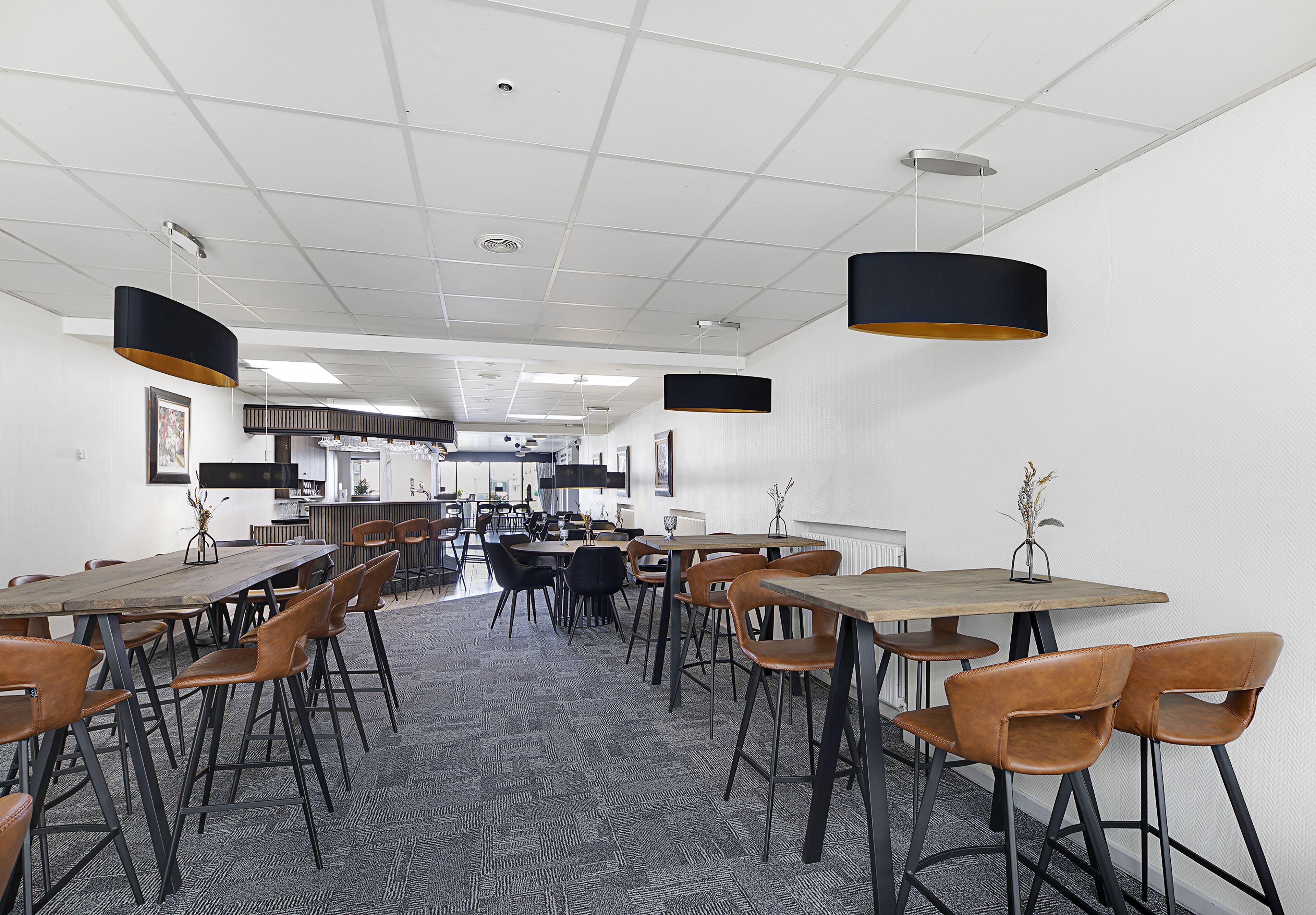 A spacious dining area with multiple tables and chairs, a patterned carpet, and pendant lighting.