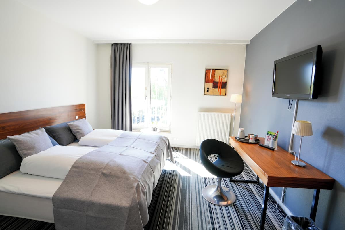 Une chambre d’hôtel avec un lit, un bureau, une chaise, une télévision et une fenêtre avec des rideaux.