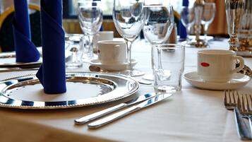 Una mesa dispuesta con platos blancos, cubiertos y cristalería transparente, incluyendo un vaso de agua y una copa de vino.