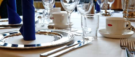 Una mesa dispuesta con platos blancos, cubiertos y cristalería transparente, incluyendo un vaso de agua y una copa de vino.