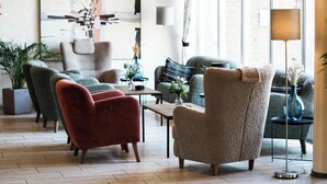 A modern living room with a sofa, armchairs, and a coffee table. There is a large abstract painting on the wall and a floor lamp. - Østergaards Hotel (Herning)