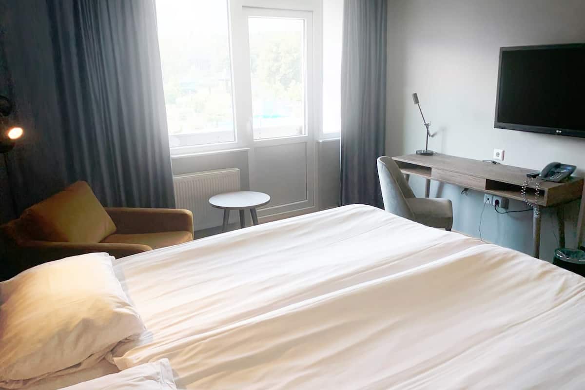 Ein Hotelzimmer mit Bett, Schreibtisch, Stuhl, Fernseher und einem Fenster mit Vorhängen.
