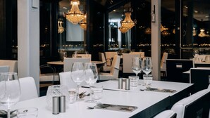 Ein Restaurantinnenraum mit gedeckten Tischen, großen Fenstern und dekorativen Kronleuchtern.