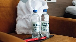 Two bottles of LOKA Naturell water on a brown sofa with a white towel and a red milk chocolate bar. - Ronneby Brunn Hotel Spa Resort (Ronneby)