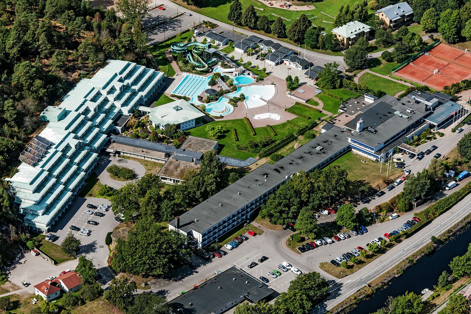 An aerial view of a hotel with multiple buildings, a swimming pool, tennis courts, and a parking lot.
