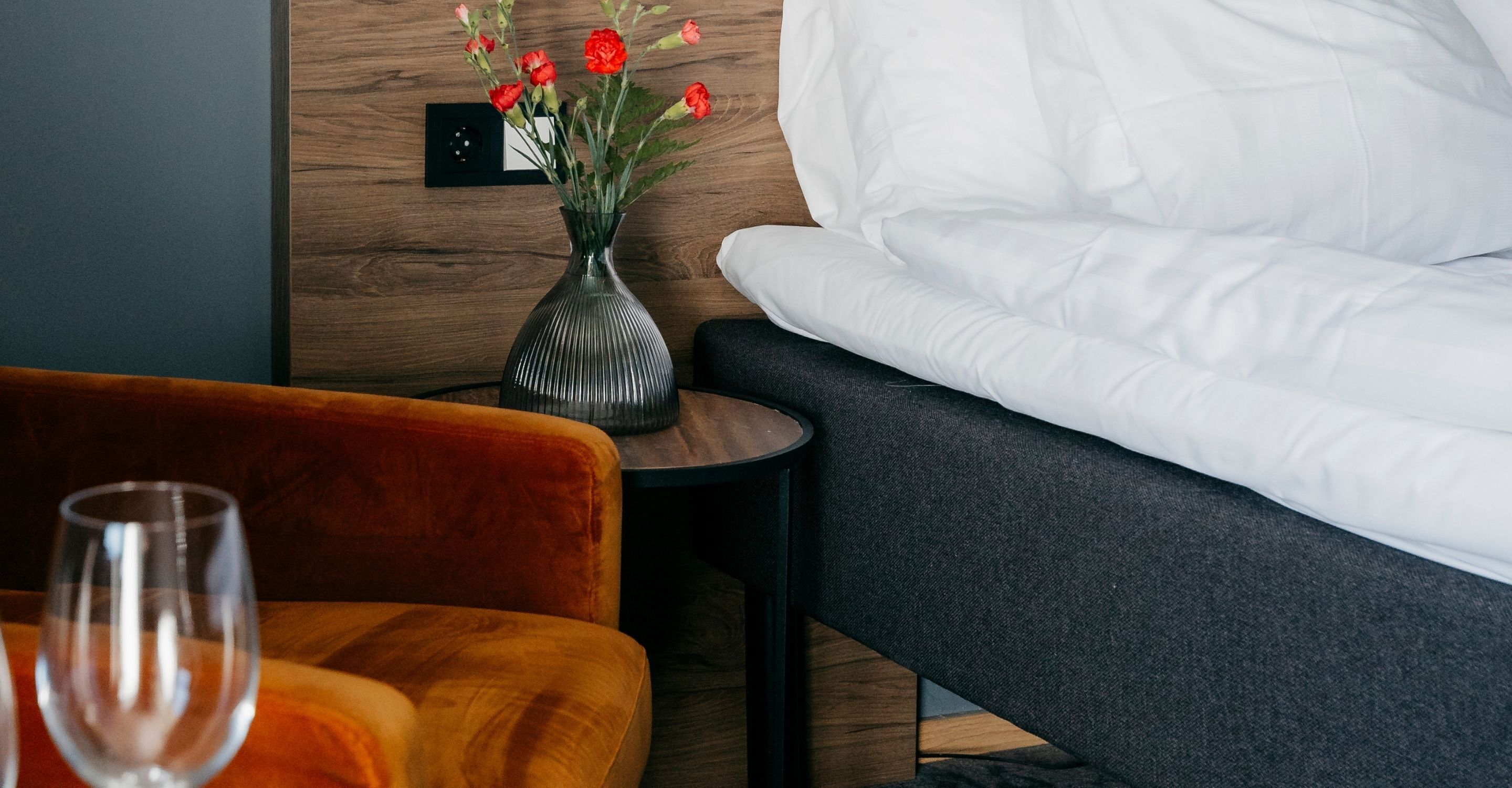 Ett hotellrum med en säng, ett litet bord med en vas med blommor och en stol.