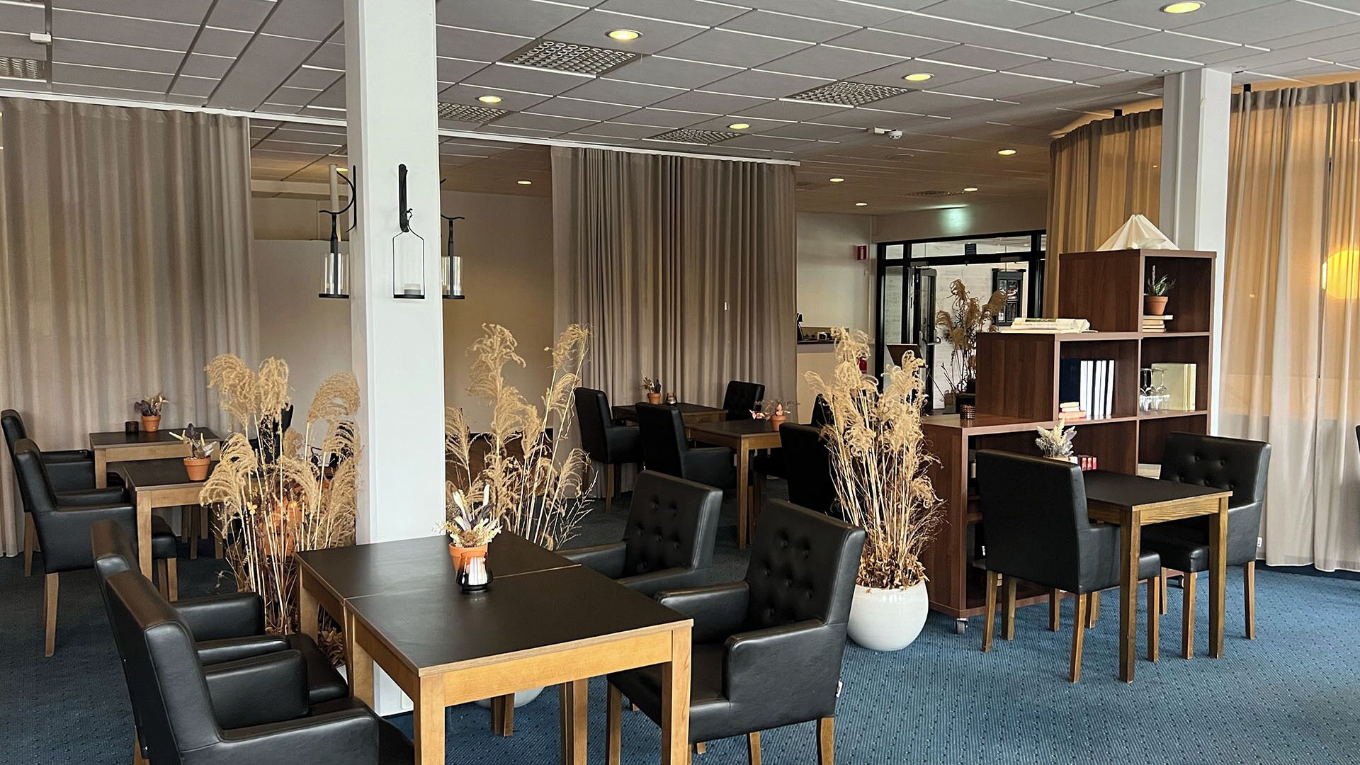 A hotel lobby with multiple seating areas, including a central dining table surrounded by chairs, and a bookshelf filled with books and decorative items.