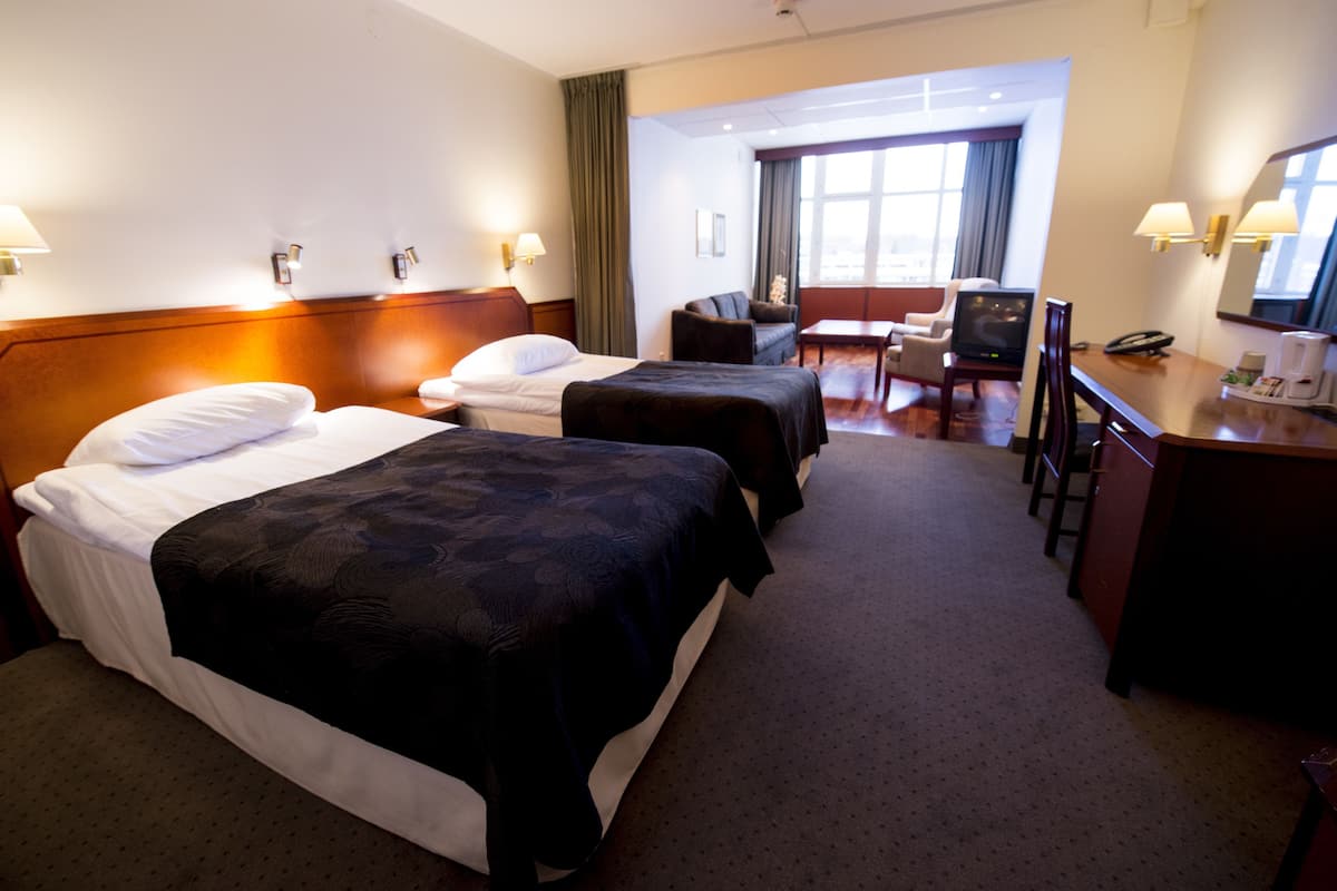 Ein Hotelzimmer mit zwei Betten, einem Schreibtisch, einem Stuhl, einem Fernseher und einem Fenster mit Vorhängen.