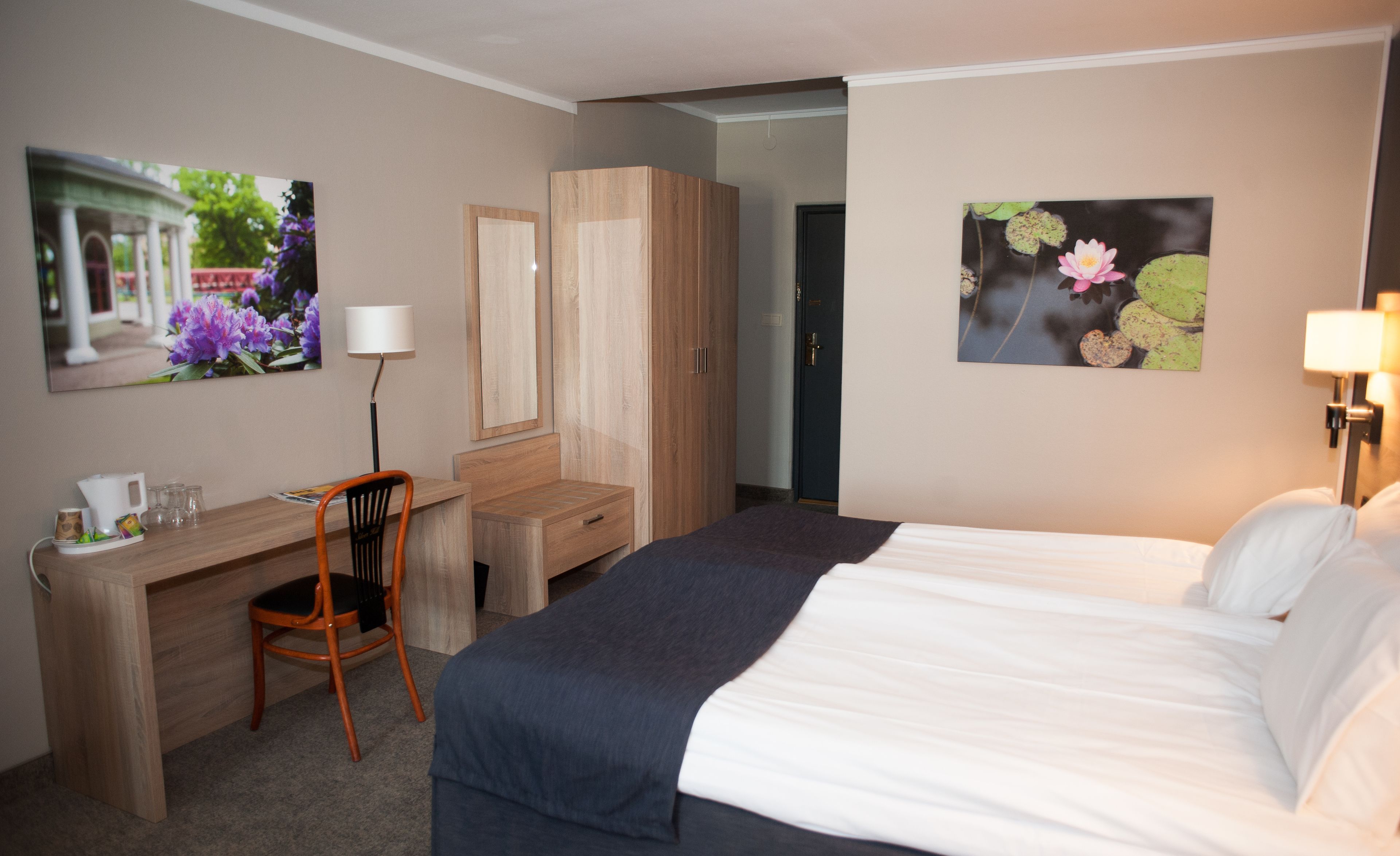 A hotel room with a bed, a desk, a chair, a wardrobe, and two wall-mounted lamps.
