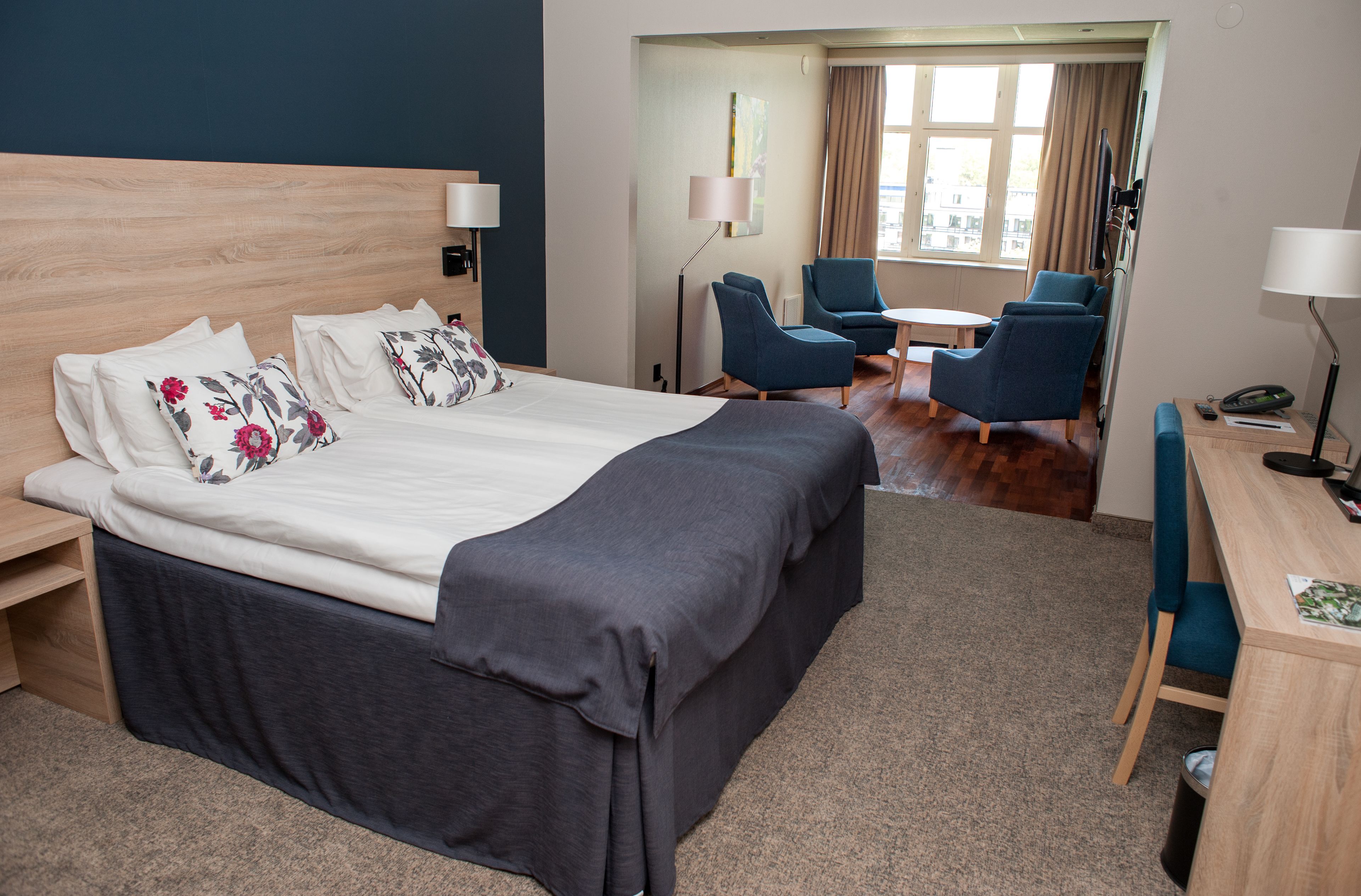 A hotel room with a large bed, bedside tables, a desk with a chair, and a small table with chairs.