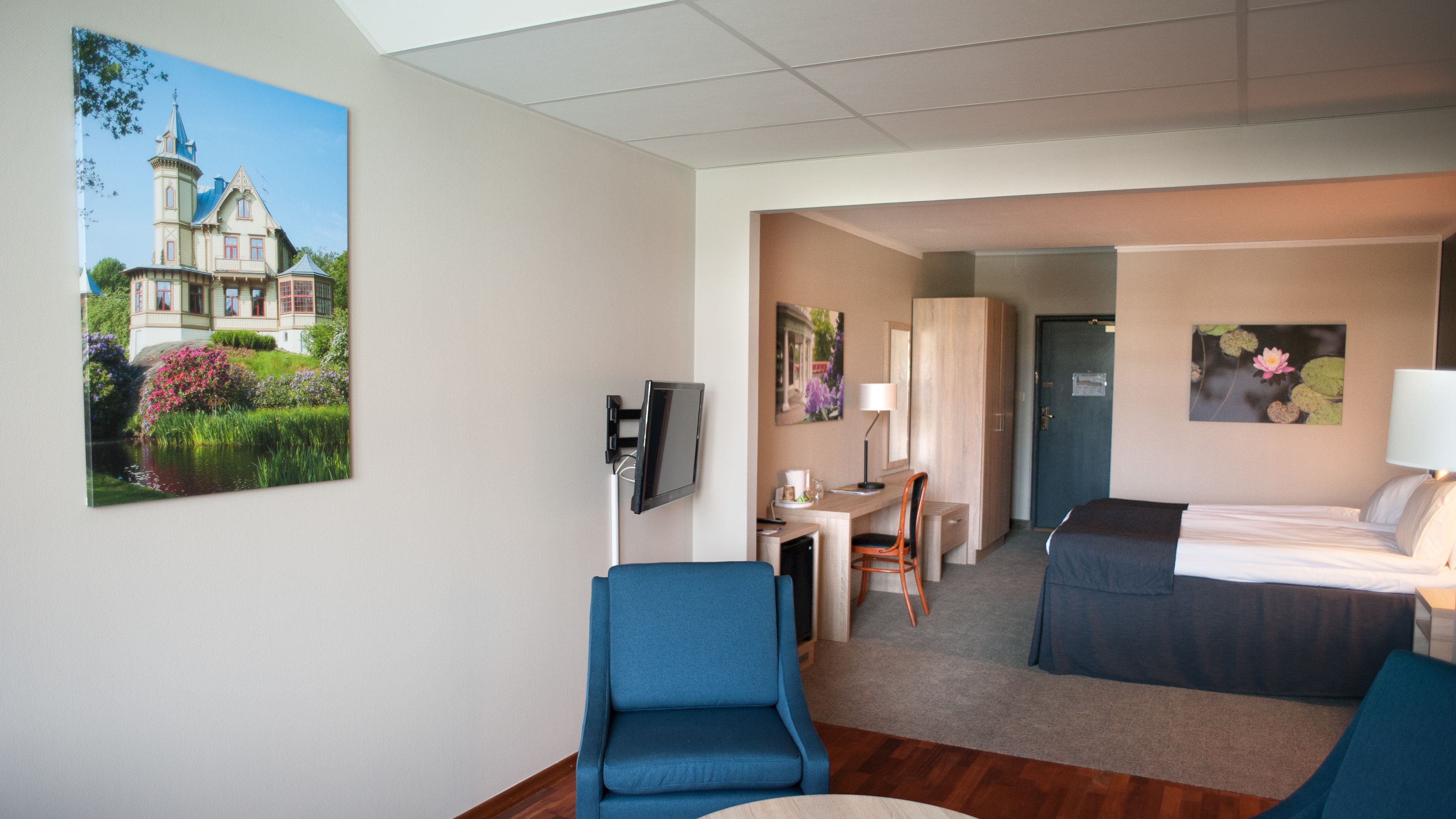 Une chambre d’hôtel avec un lit, un bureau et une chaise, une télévision et un tableau représentant un château.