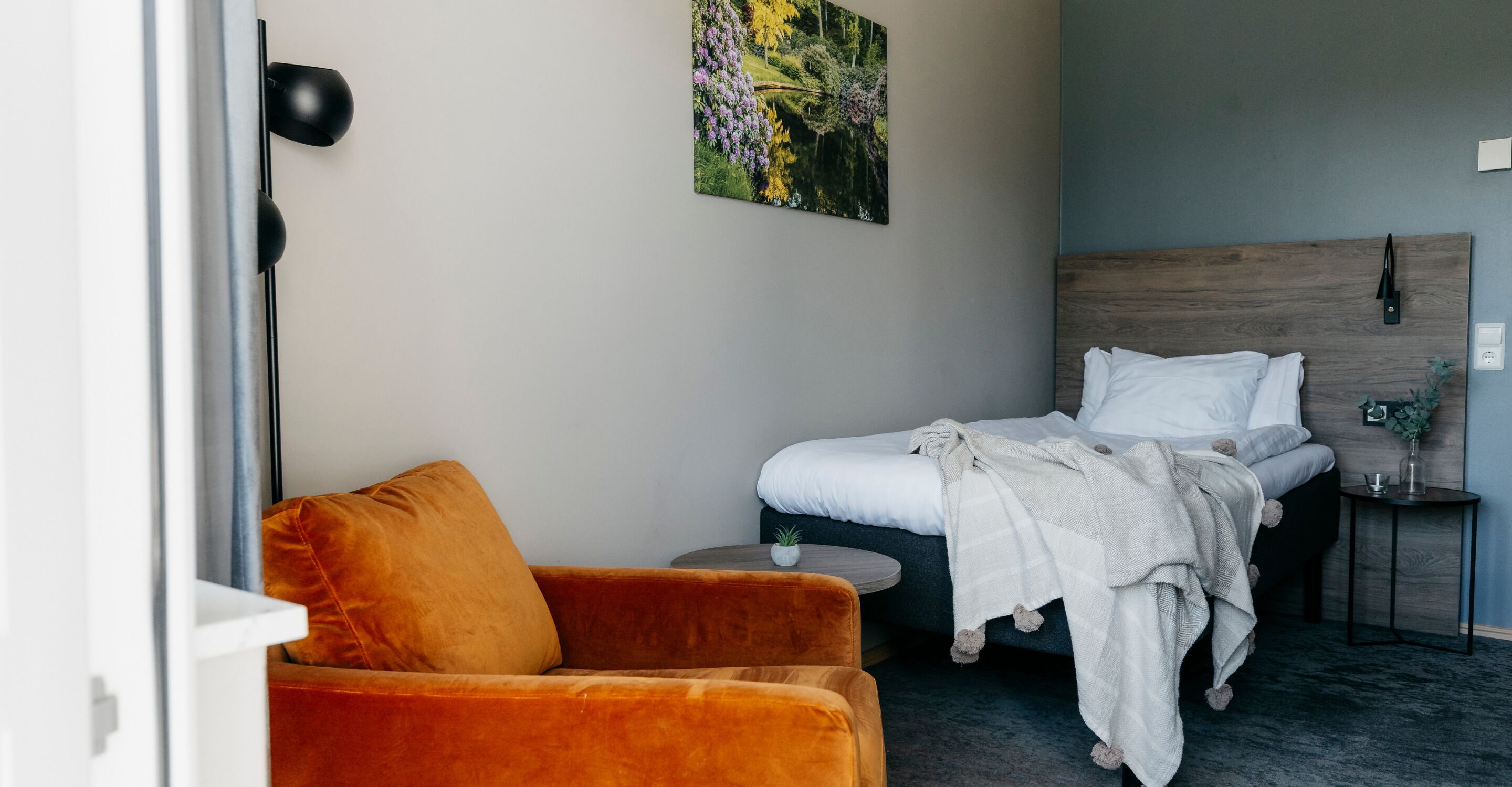 Un dormitorio con cama, una mesita redonda pequeña, una silla y un cuadro en la pared.
