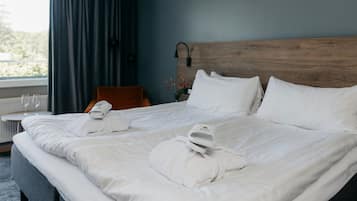 Camera d'albergo con un letto grande, due cuscini, una testiera in legno, un comodino con una lampada e una finestra con tende.