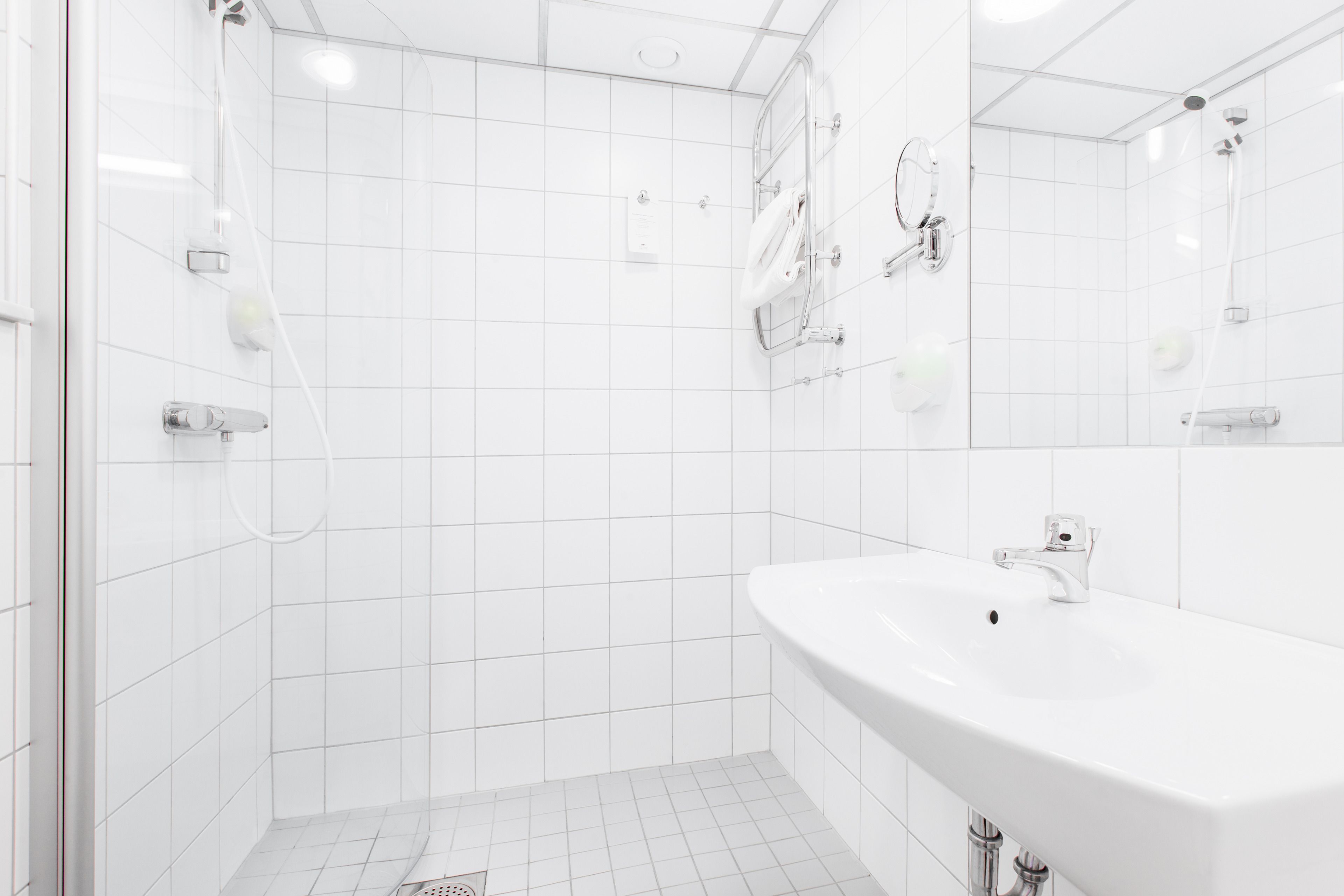 Ein modernes Badezimmer mit weißen Fliesen, einem großzügigen Waschbecken und einer Duschkabine.