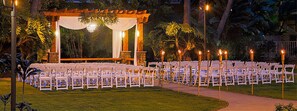 Un lieu de réception en plein air pour les mariages, avec des rangées de chaises blanches et une arche en bois.
