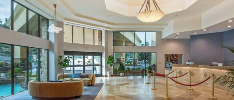 A spacious lobby with a large seating area, a reception desk, and large windows offering views of the outdoors.