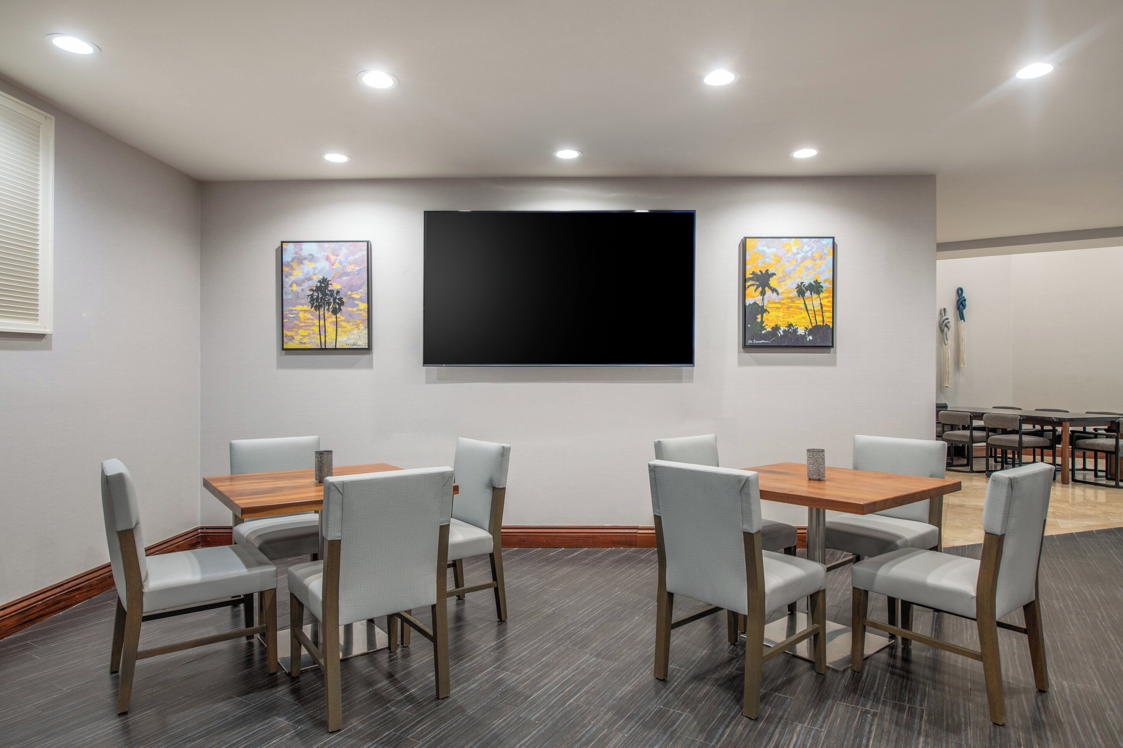 Un salón de conferencias con una televisión de pantalla grande, sillas blancas y una mesa de madera.