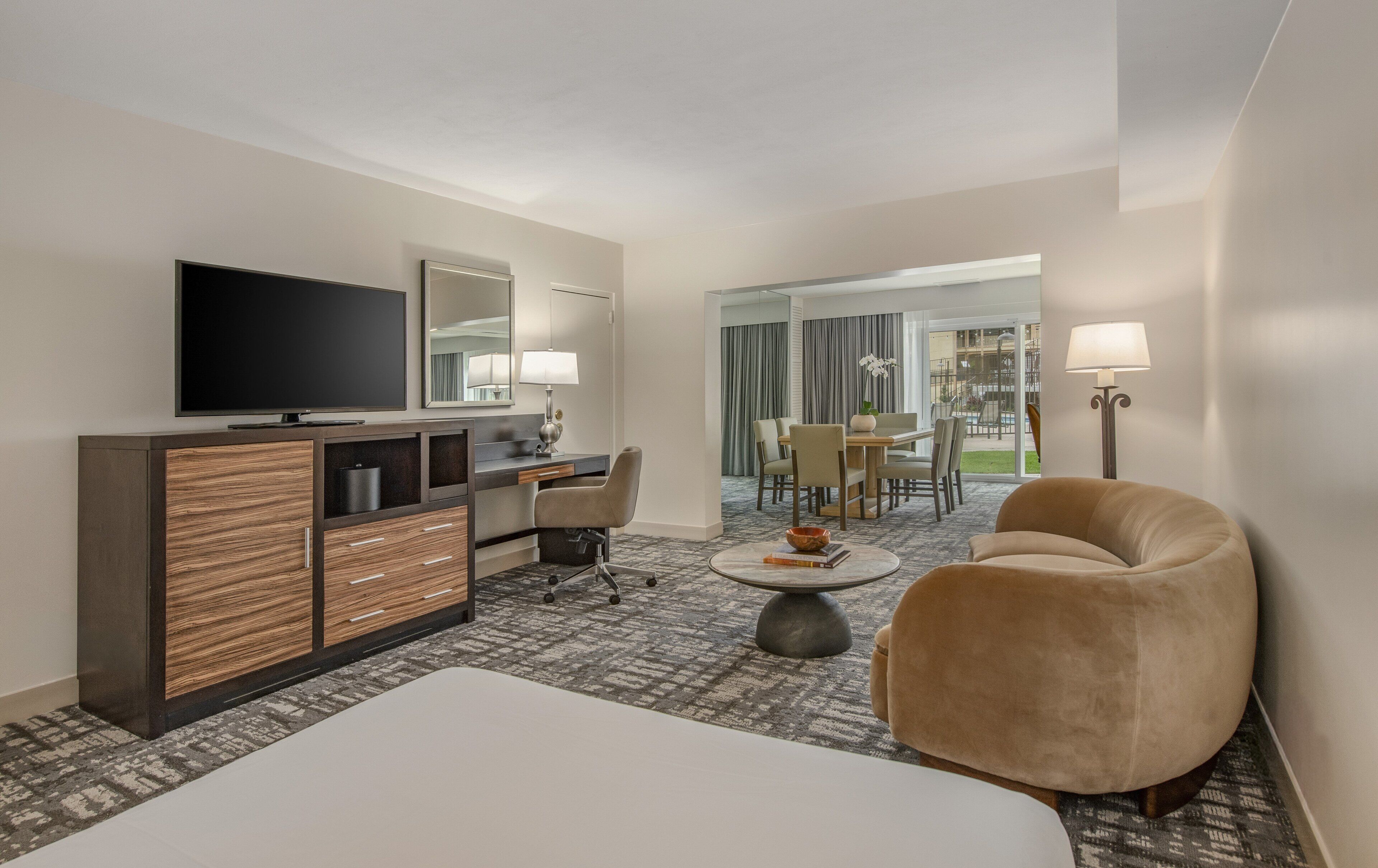 A hotel room with a bed, a TV, a desk with a chair, a sofa, and a view of the outside.