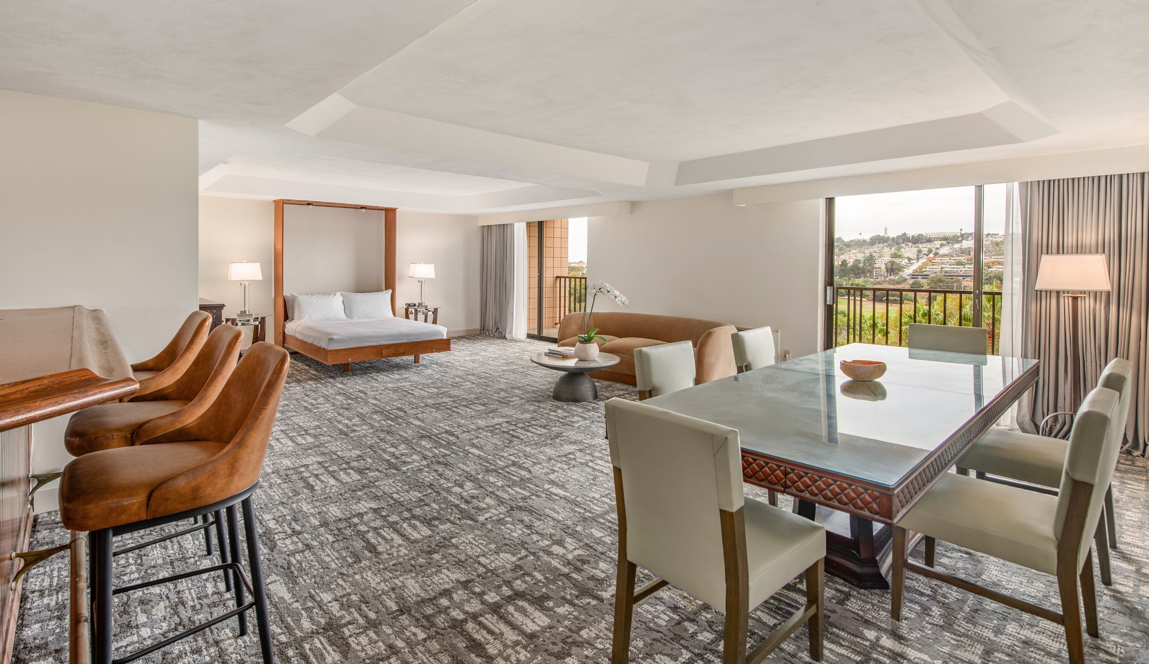A hotel room with a bed, a sofa, a dining table, and a balcony with a view.