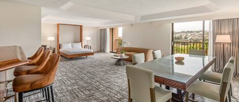 A hotel room with a bed, a sofa, a dining table, and a balcony with a view.