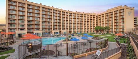 A hotel with a large pool area, outdoor seating, and a well-maintained garden.