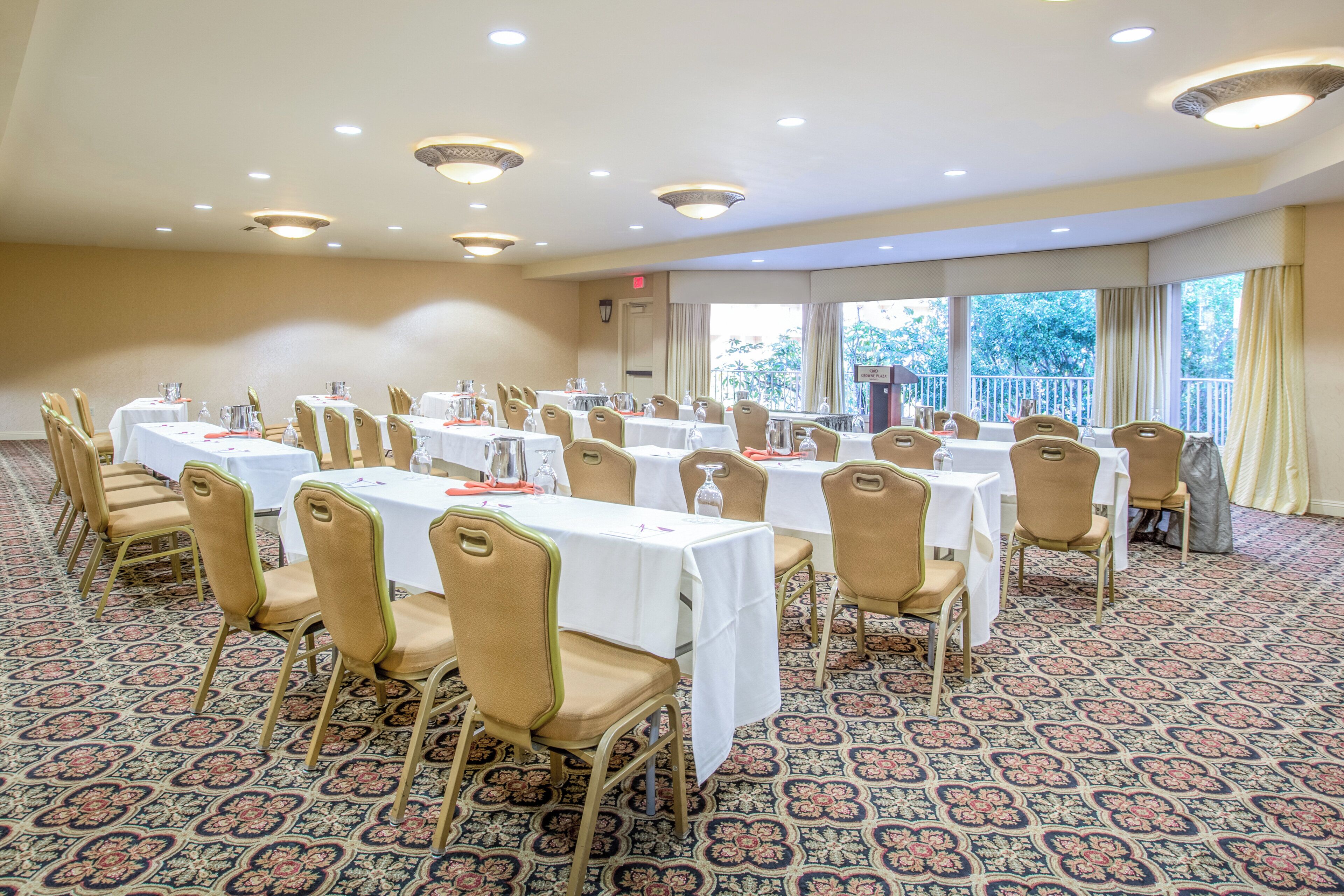 A conference room with multiple tables and chairs, carpeted floor, and large windows with curtains.