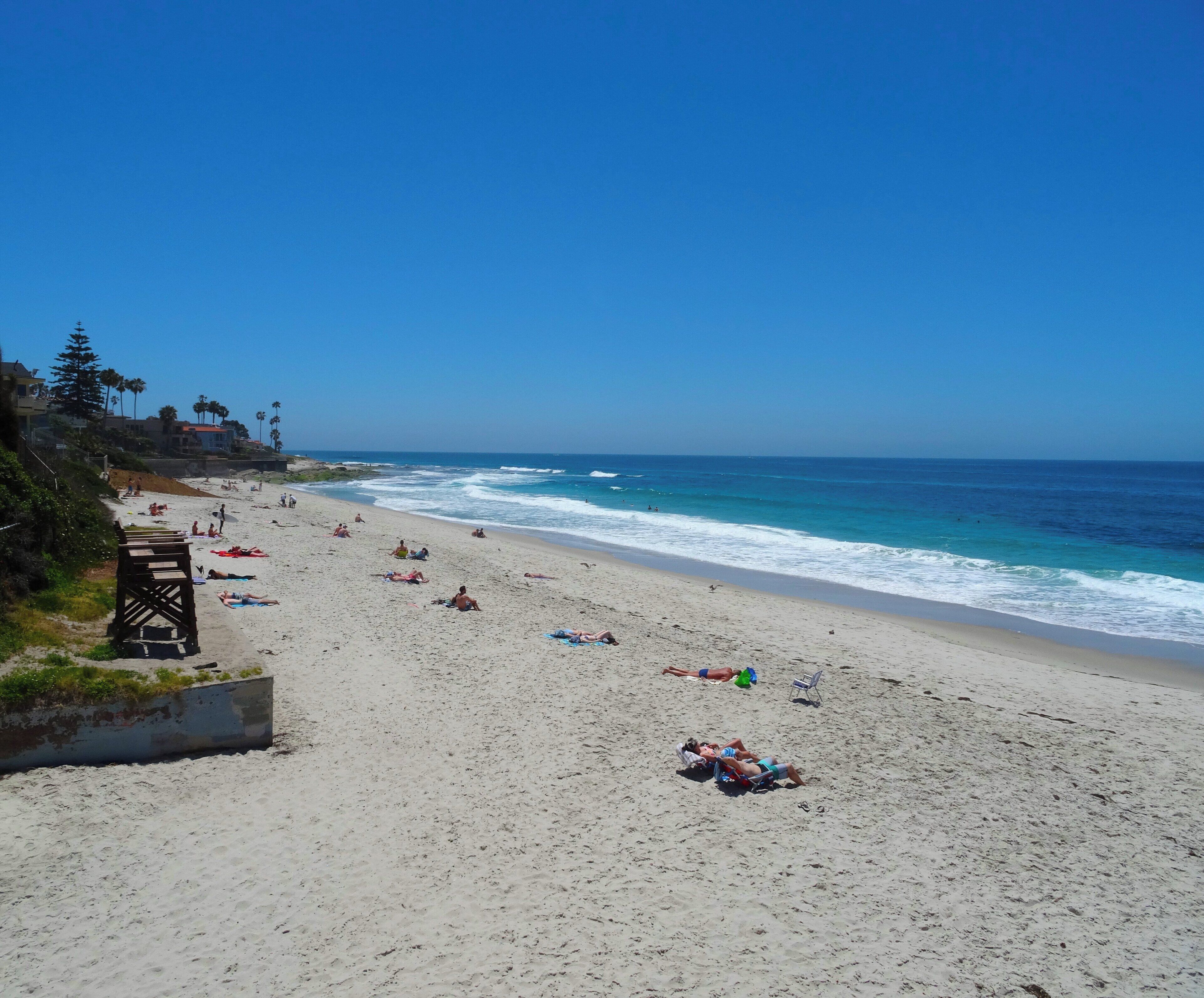 A beach with people sunbathing and swimming, a clear sky, and ocean waves.