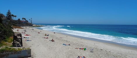 A beach with people sunbathing and swimming, a clear sky, and ocean waves.
