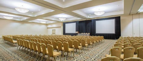 Un salón de conferencias con filas de sillas, un escenario con pantalla y una alfombra estampada.