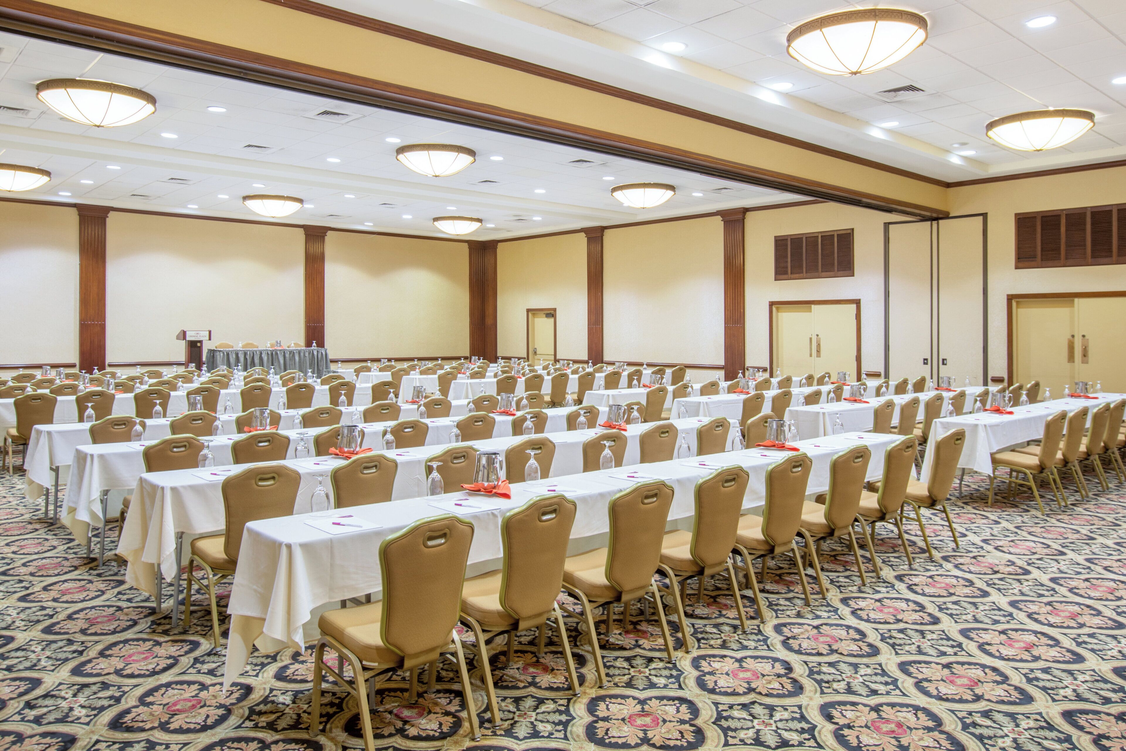 A large conference room with rows of tables and chairs, equipped with water bottles and nameplates.