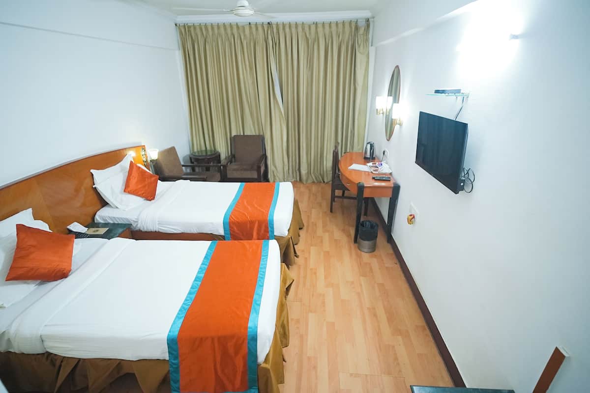 A hotel room with two beds, a desk, a chair, a TV, and a curtain.