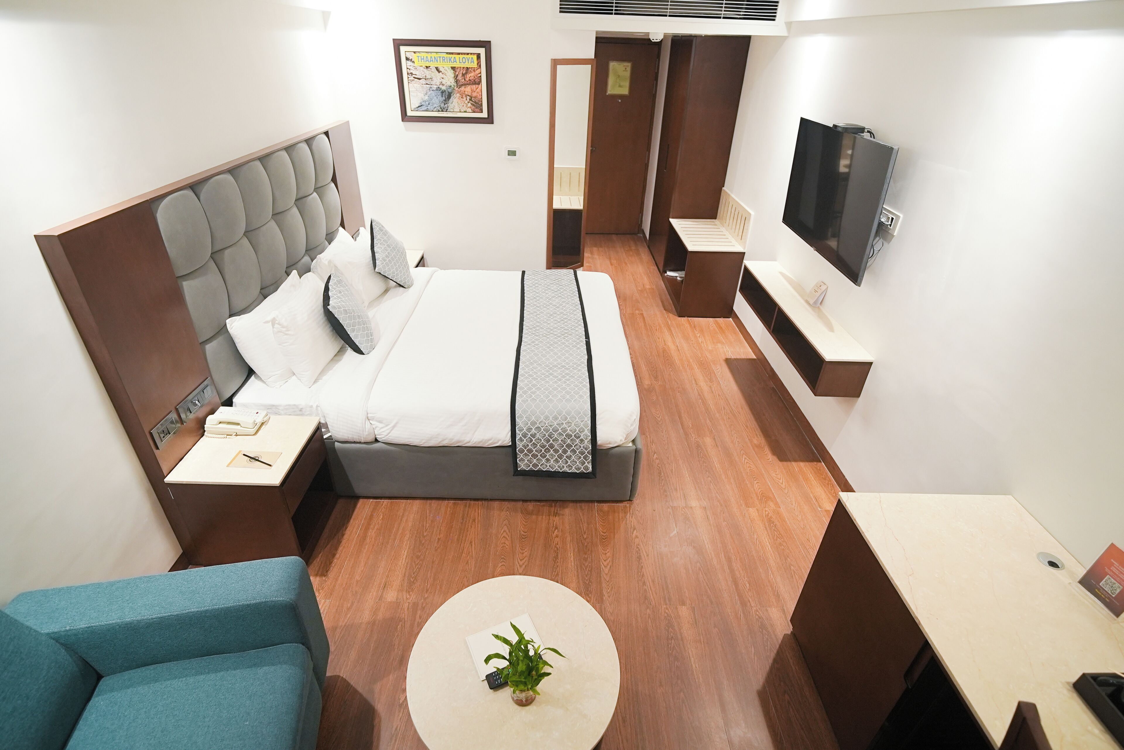 A hotel room with a bed, bedside tables, a TV, a desk, a chair, and a small table with a plant.