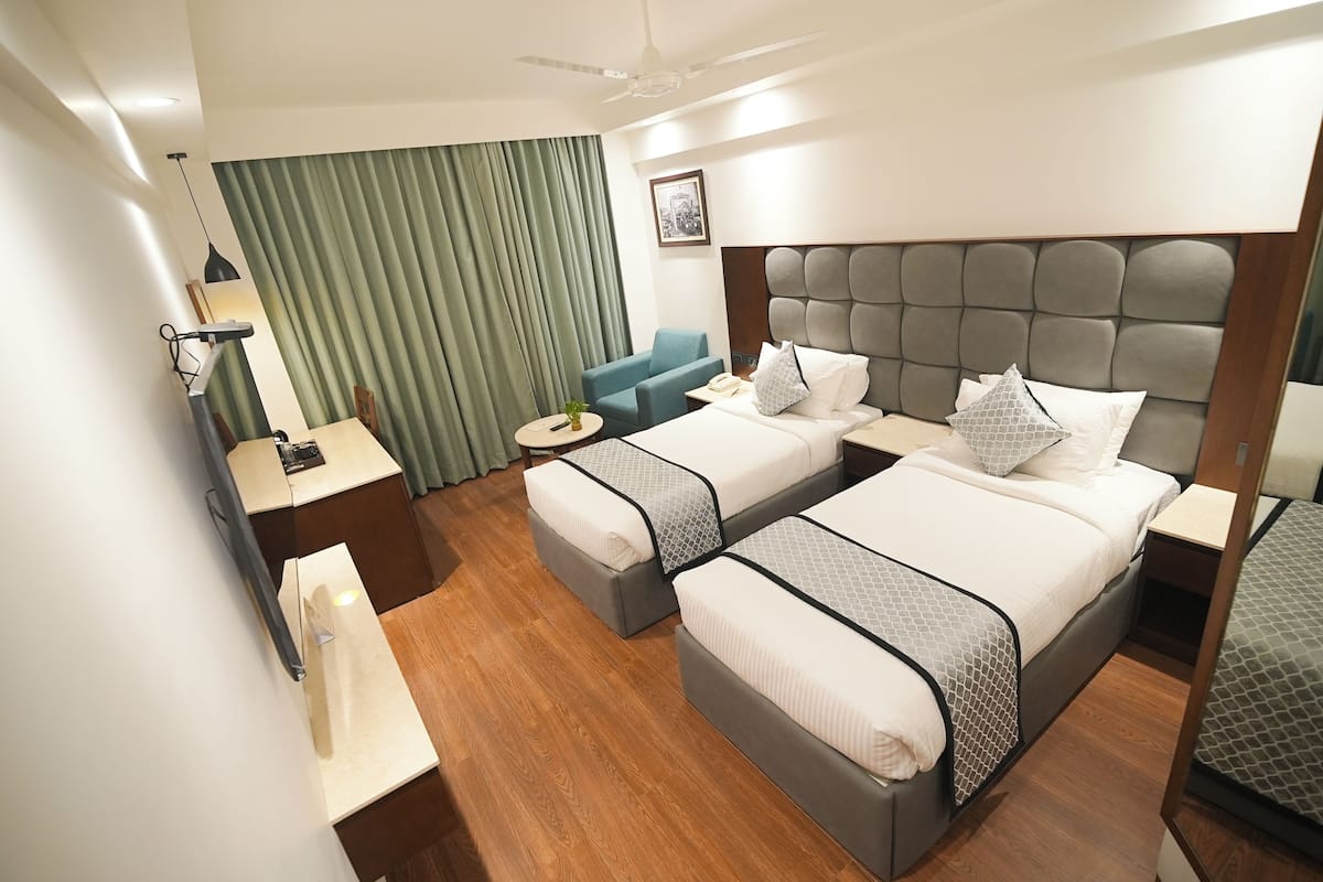 A hotel room with two beds, a desk, a chair, a ceiling fan, and a large window with curtains.