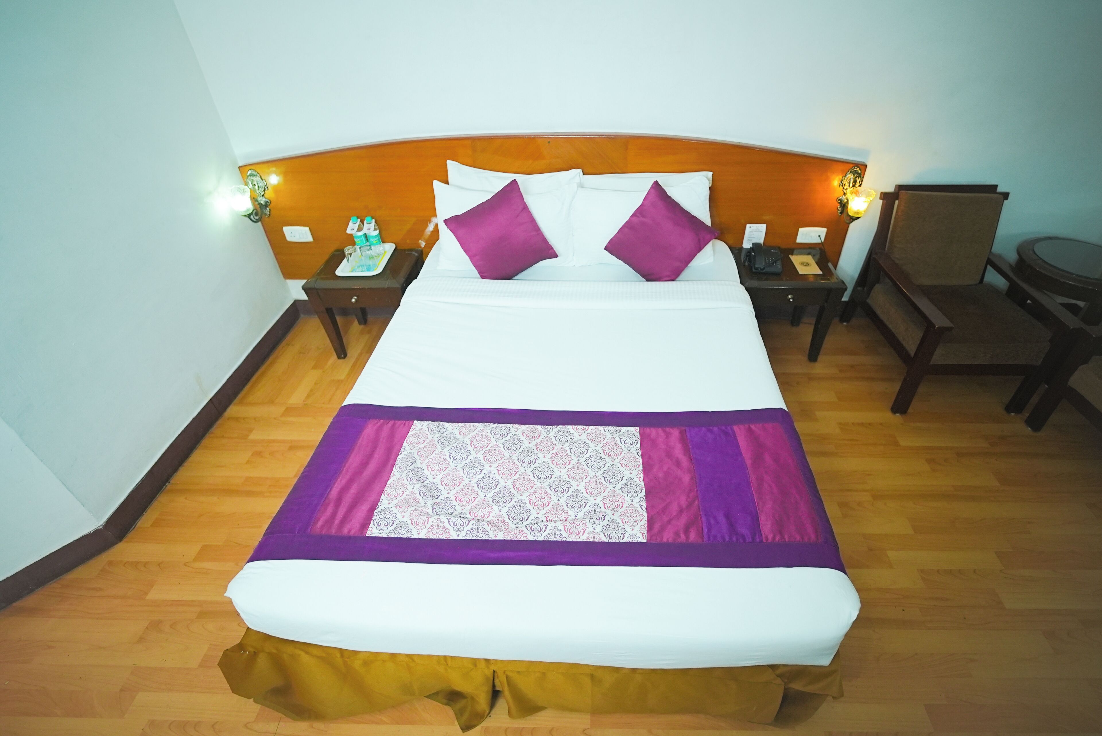 A hotel room with a large bed, a nightstand with a lamp, a chair, and a small table.