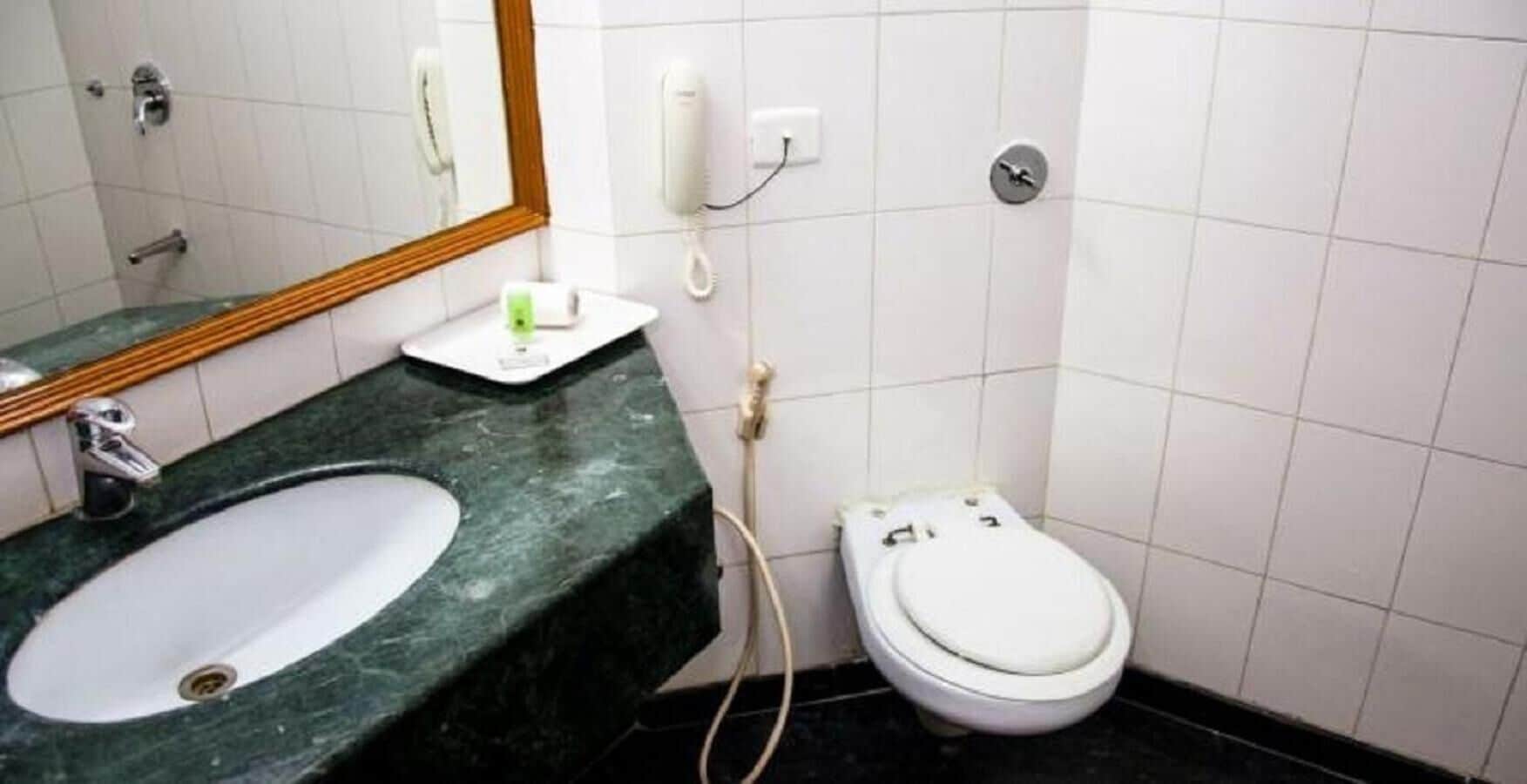 A bathroom with a white toilet, a sink with a green countertop, and a mirror above the sink.