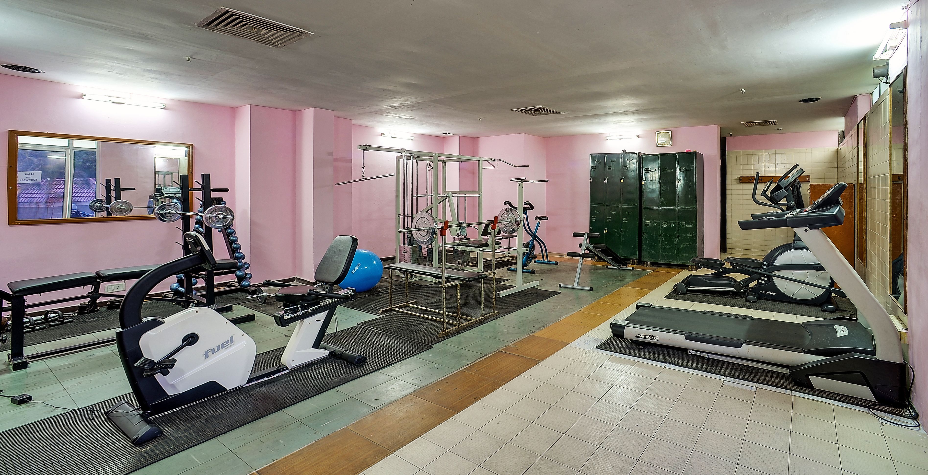 A gym with pink walls, various exercise equipment, and a mirrored wall.