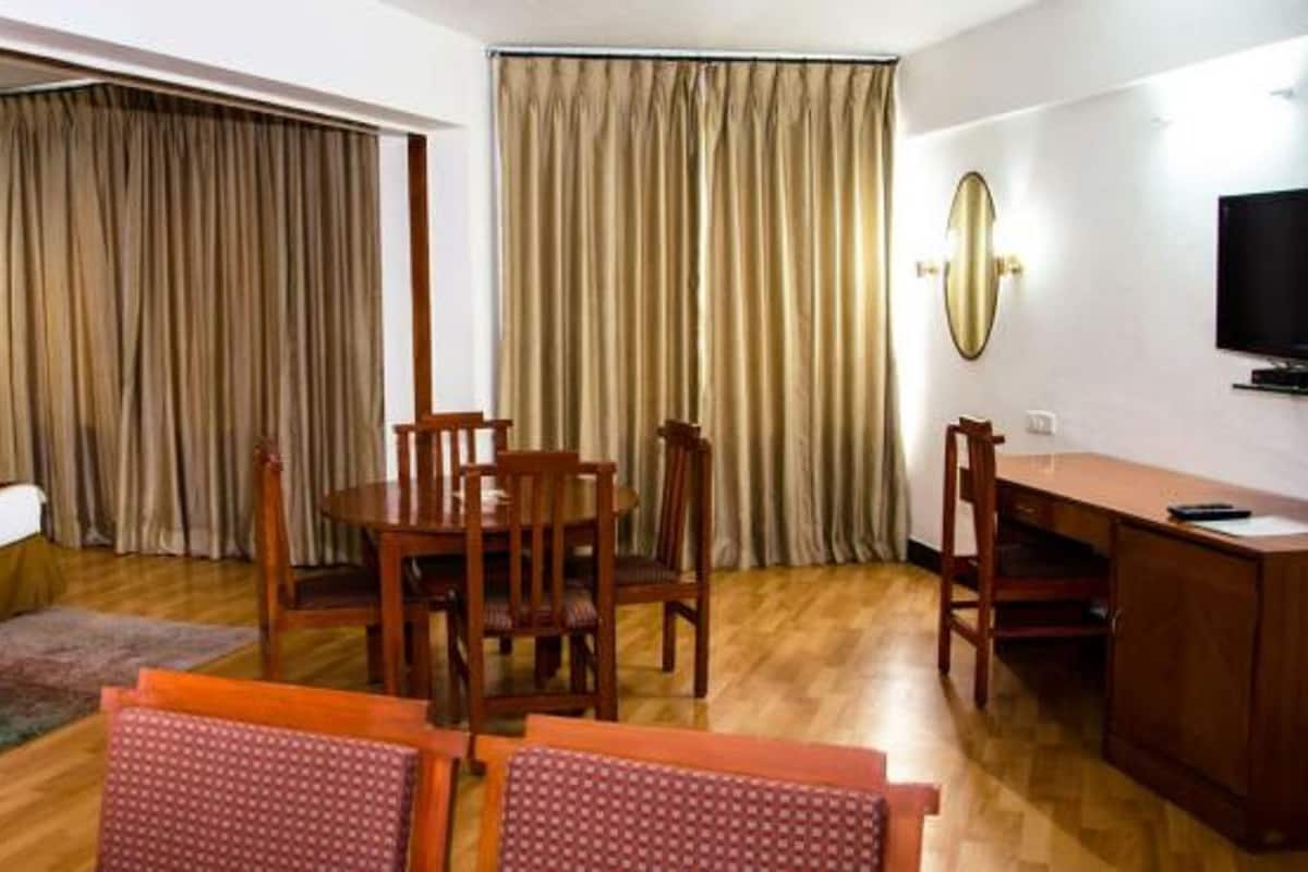 A hotel room with a bed, a desk, a chair, a dining table, and curtains.