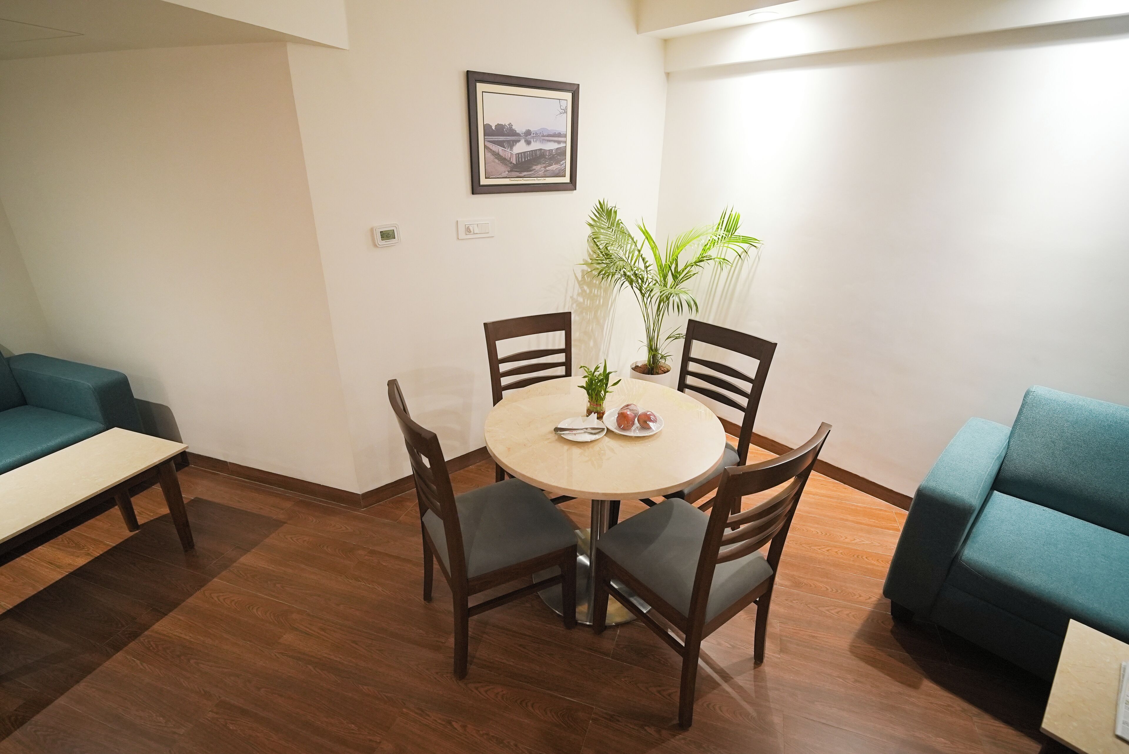 Un comedor con una mesa redonda, cuatro sillas, una planta en maceta y un cuadro en la pared.