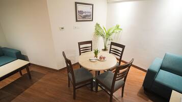 A dining area with a round table, four chairs, a potted plant, and a framed picture on the wall.