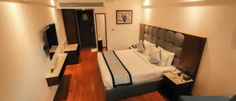 A modern hotel room with a large bed, bedside tables, a TV, and a seating area.