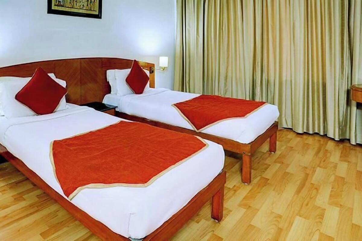 A hotel room with two beds, wooden headboards, white bedding, red throw pillows, a wooden floor, and a curtain.