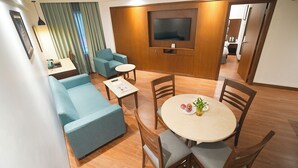 A modern living room with a sofa, a dining table with chairs, a TV mounted on the wall, and a small table with a plant.